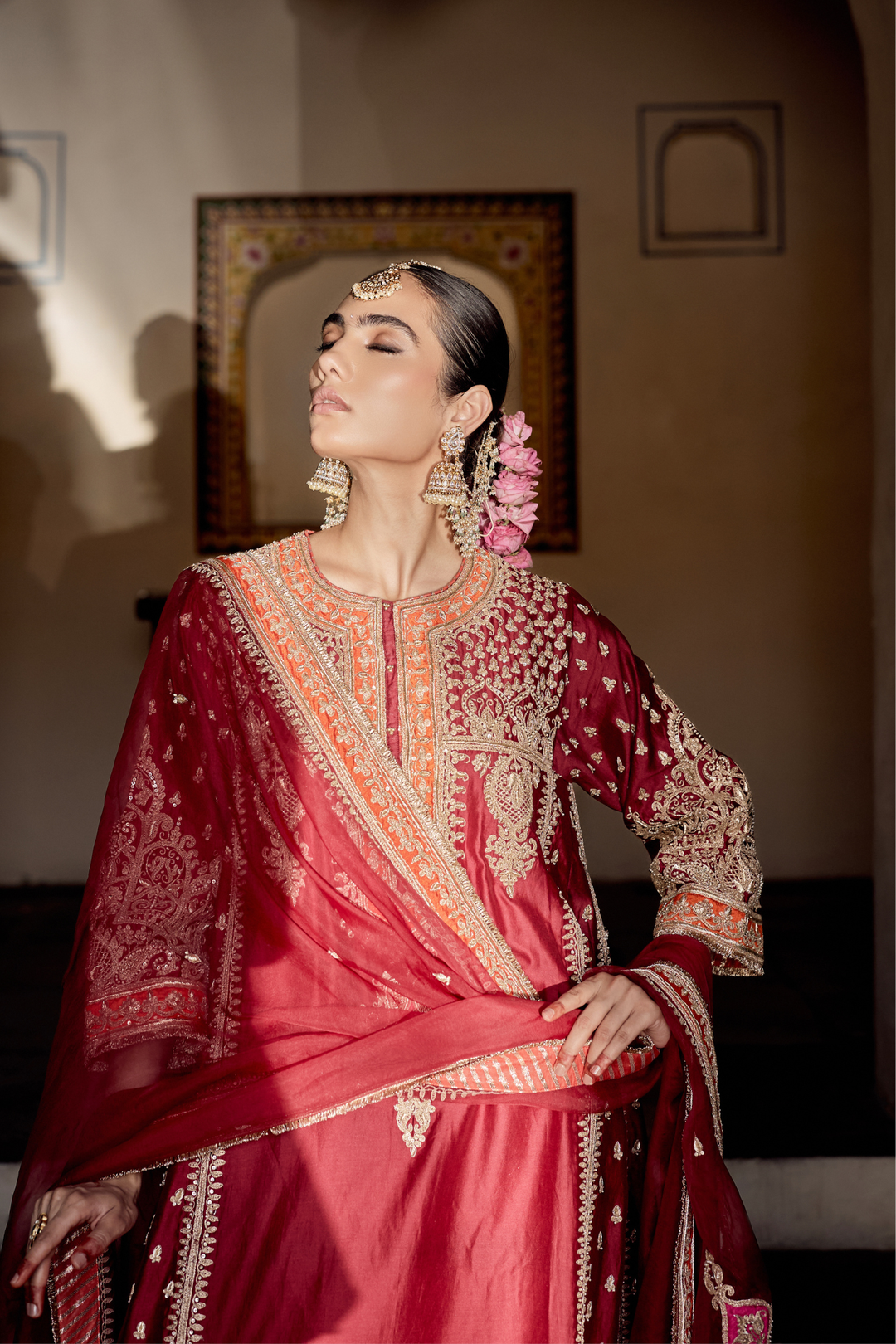 Woman in a red traditional outfit with intricate patterns and jewelry indoors.