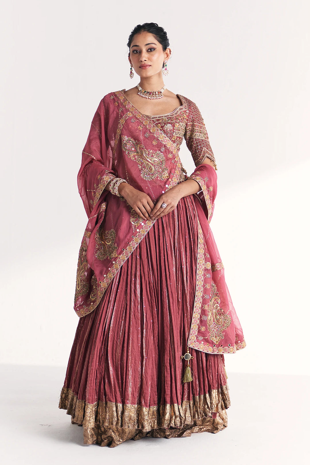 Woman wearing a traditional pink and gold embroidered Lehenga Set on a white background