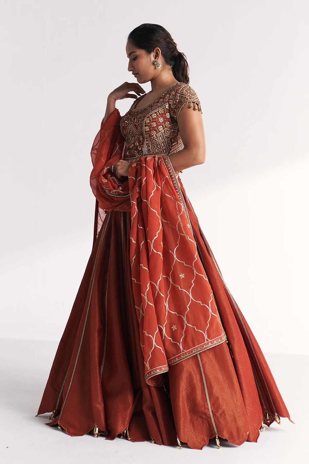 Woman wearing a traditional orange and gold Lehenga Set on a white background