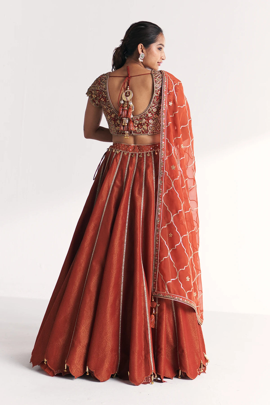 Woman wearing a traditional orange Lehenga Set with intricate patterns on a white background