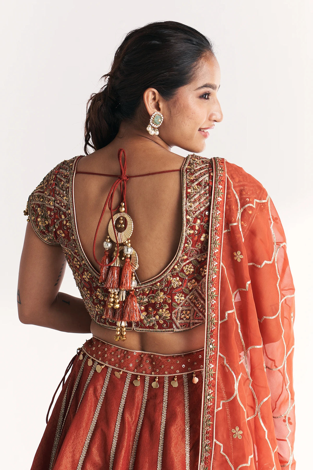 Woman wearing a traditional orange and gold embroidered Lehenga Set with a plain background