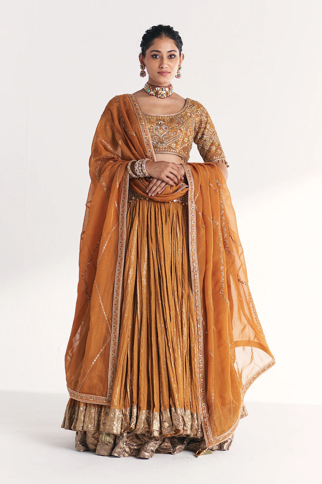Woman wearing a traditional orange and gold Lehenga with a white background