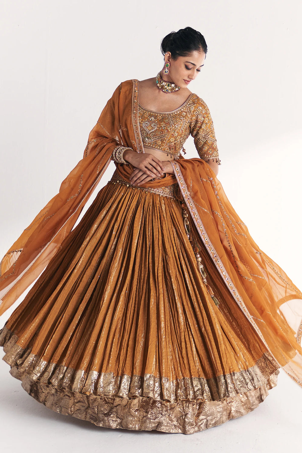 Woman wearing a traditional orange and gold Lehenga with a flowing dupatta on a white background