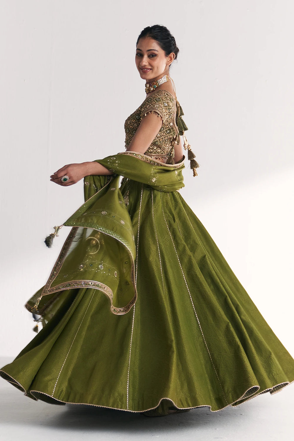 Woman wearing a green traditional Lehenga Set with a gold blouse on a white background