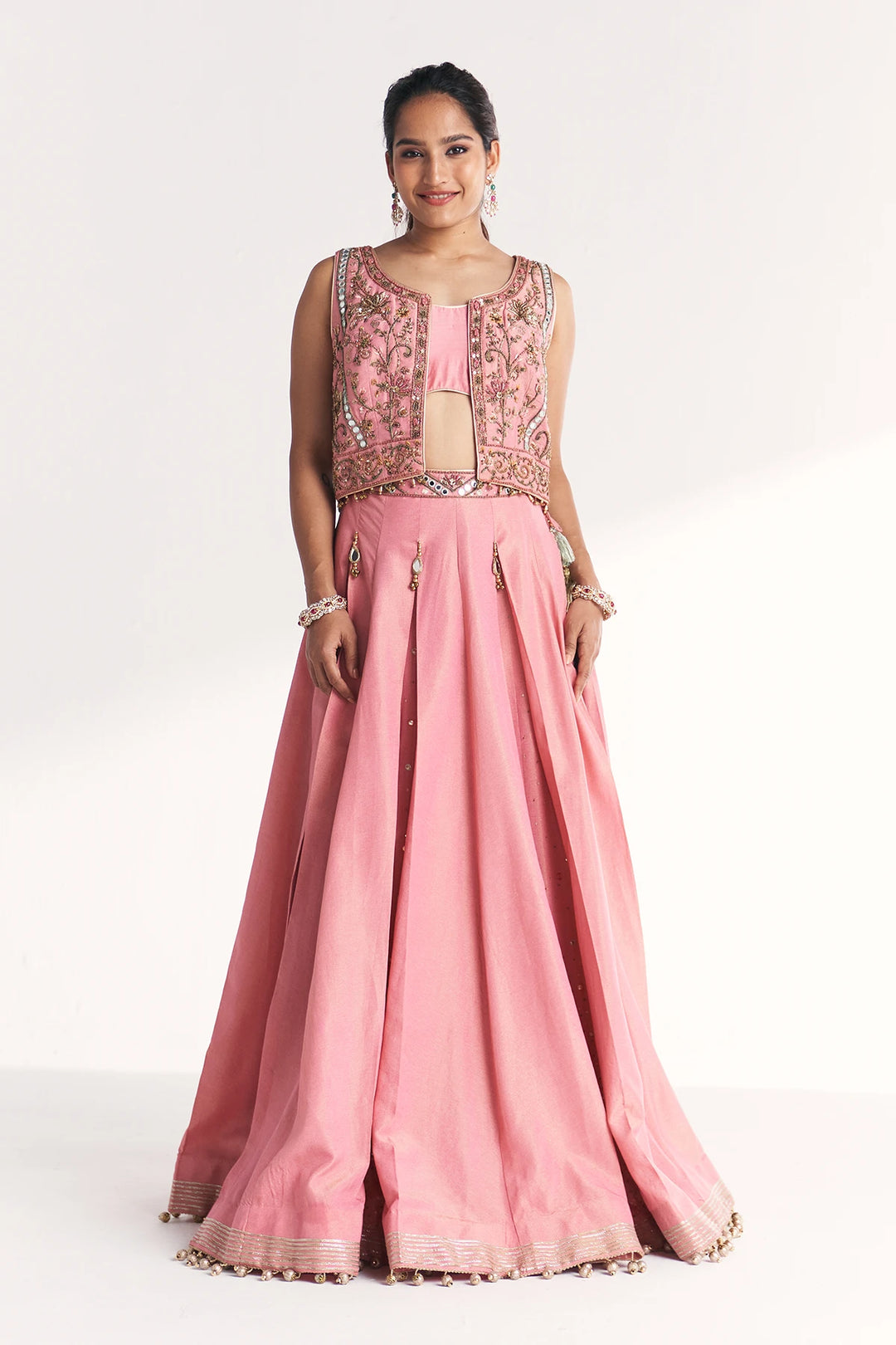 Woman wearing a pink traditional Lehenga Set with intricate designs on a white background