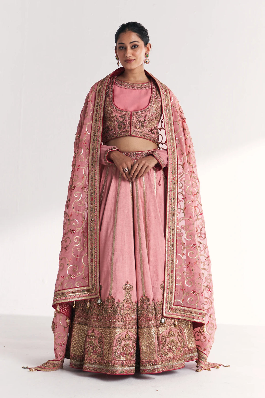 Woman wearing a traditional pink and gold embroidered Lehenga Set on a white background