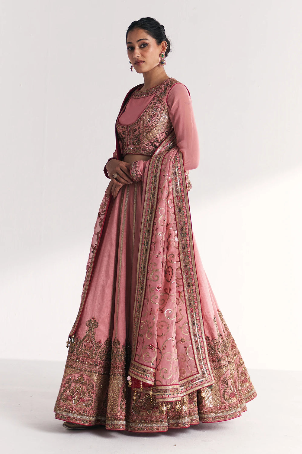 Woman wearing a traditional pink and gold embroidered Lehenga Set on a white background