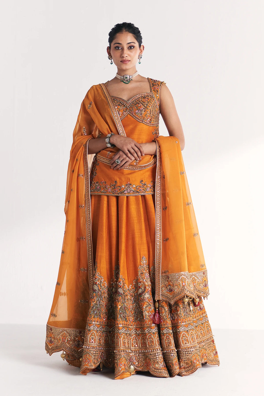 Woman wearing an orange traditional Lehenga Set with intricate patterns on a white background