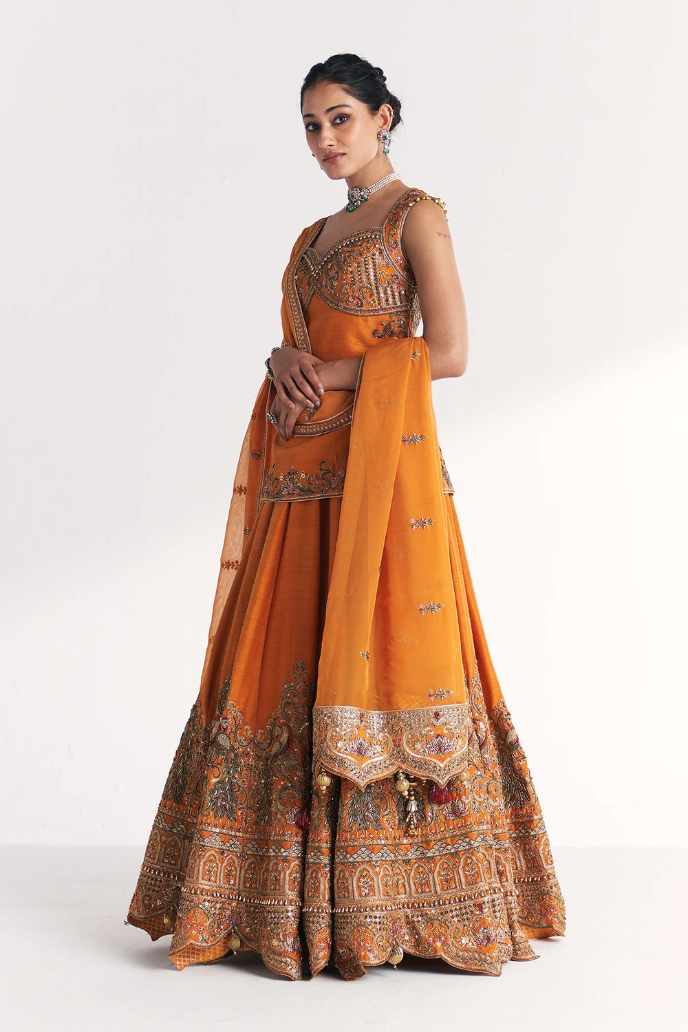 Woman wearing an orange traditional Lehenga Set with intricate patterns on a white background