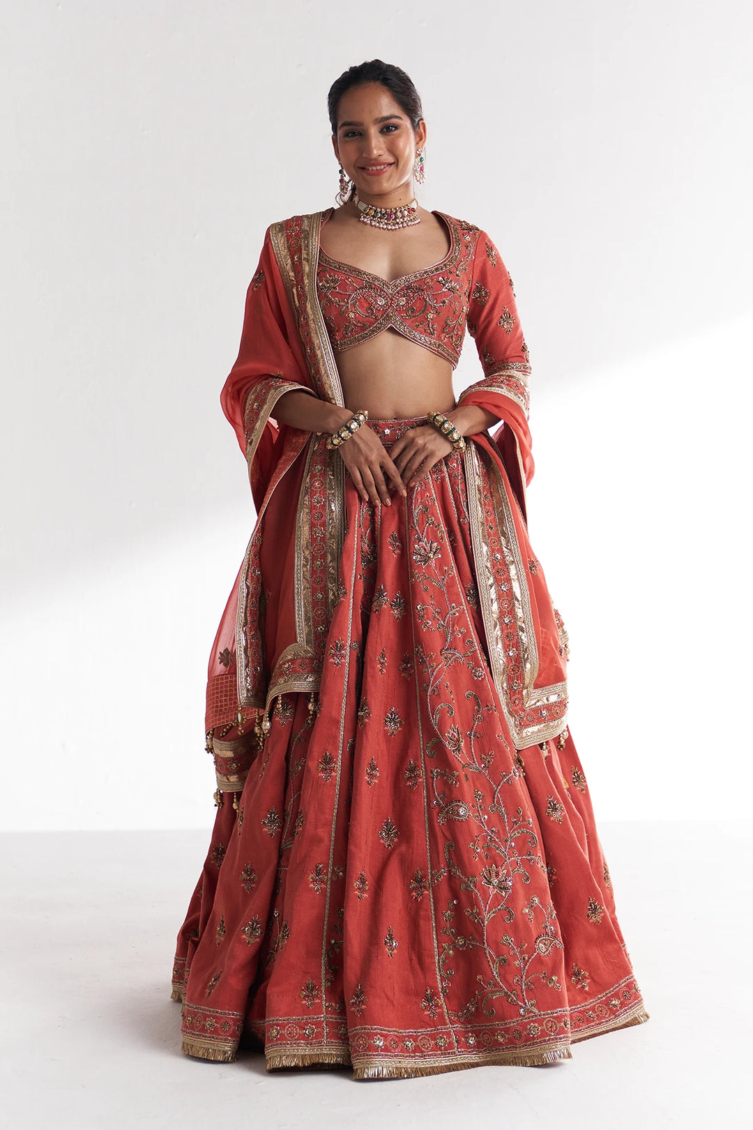 Woman wearing a traditional red and gold embroidered Lehenga Set on a white background