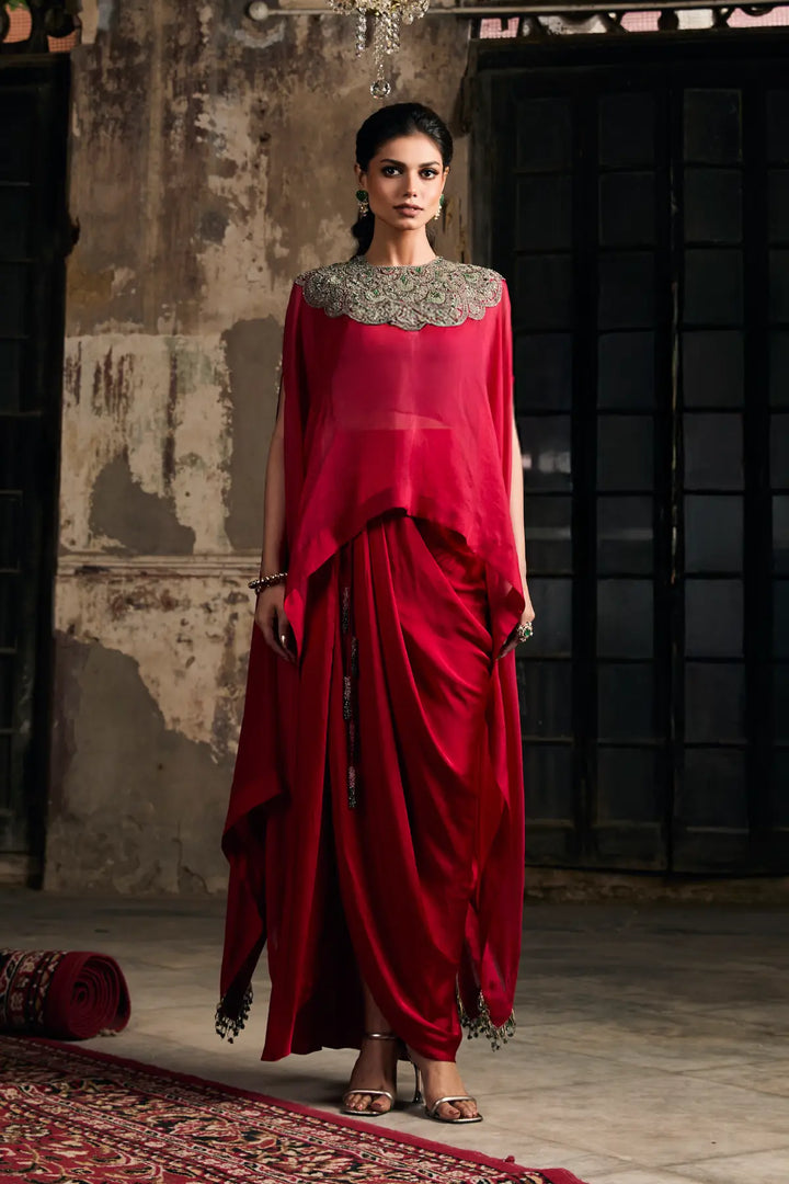 Woman wearing a red kaftan with a textured blouse against a rustic wall.
