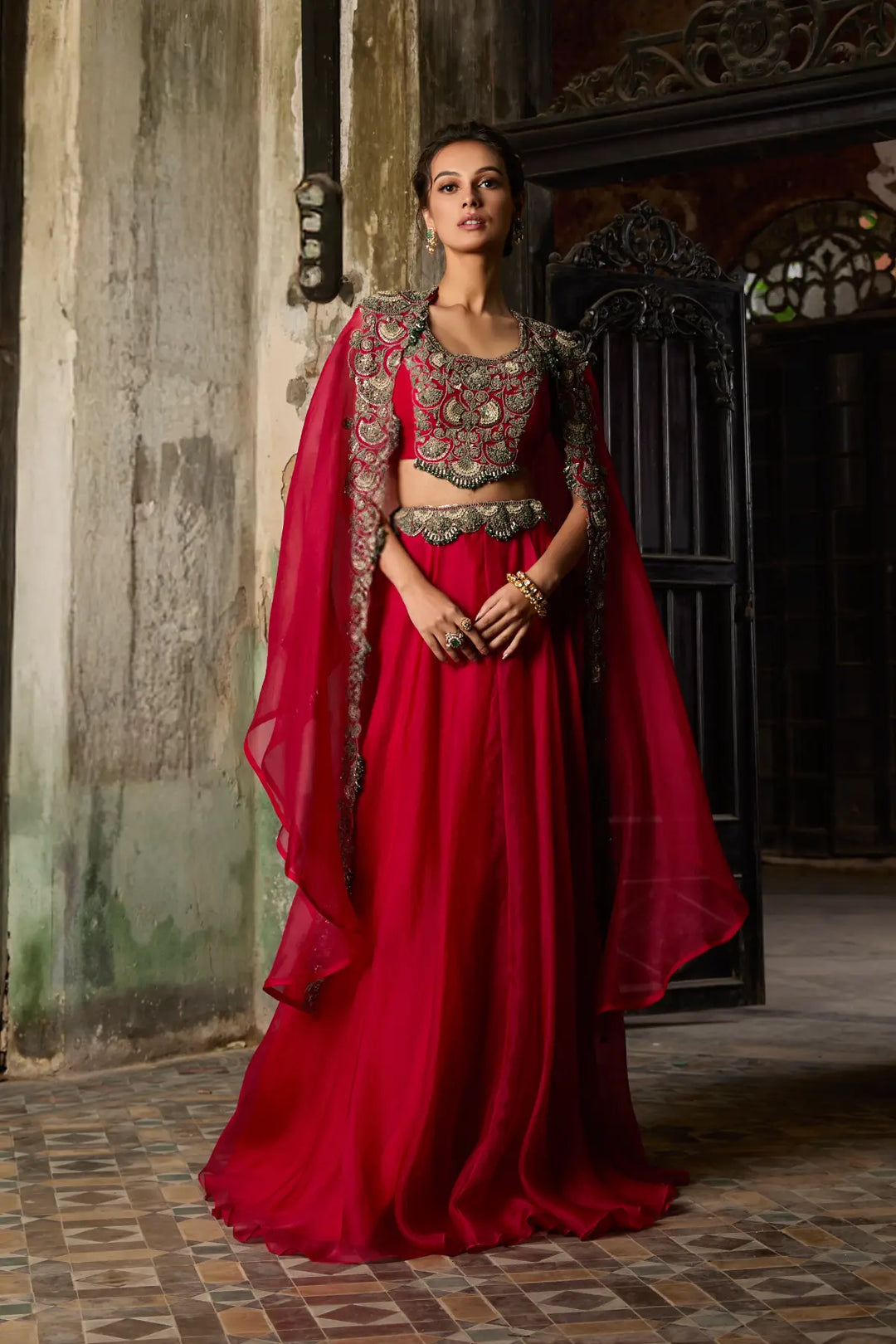Woman in a red traditional cape and skirt with intricate designs standing in a dimly lit room.