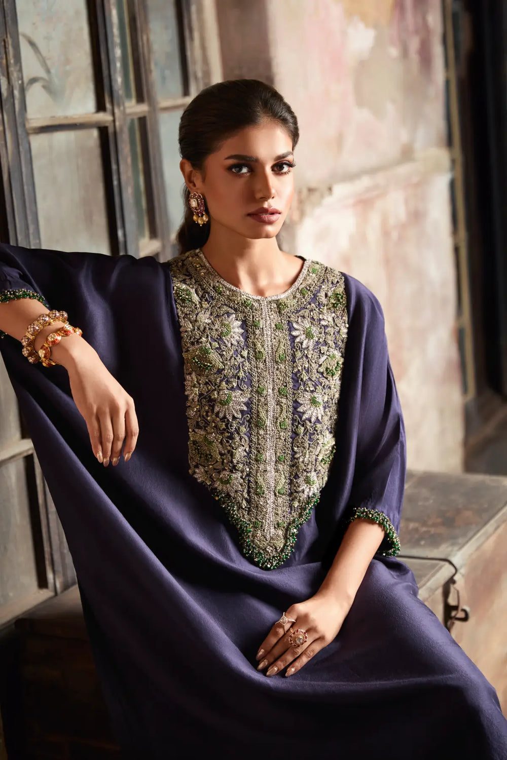 Woman wearing a dark blue traditional kaftan with floral embroidery in an indoor setting.