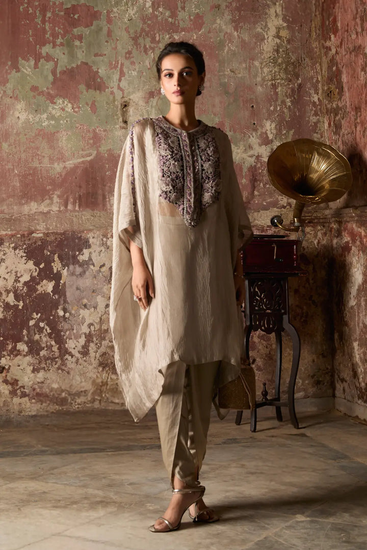 Woman in traditional kaftan standing next to a vintage gramophone against a textured wall.