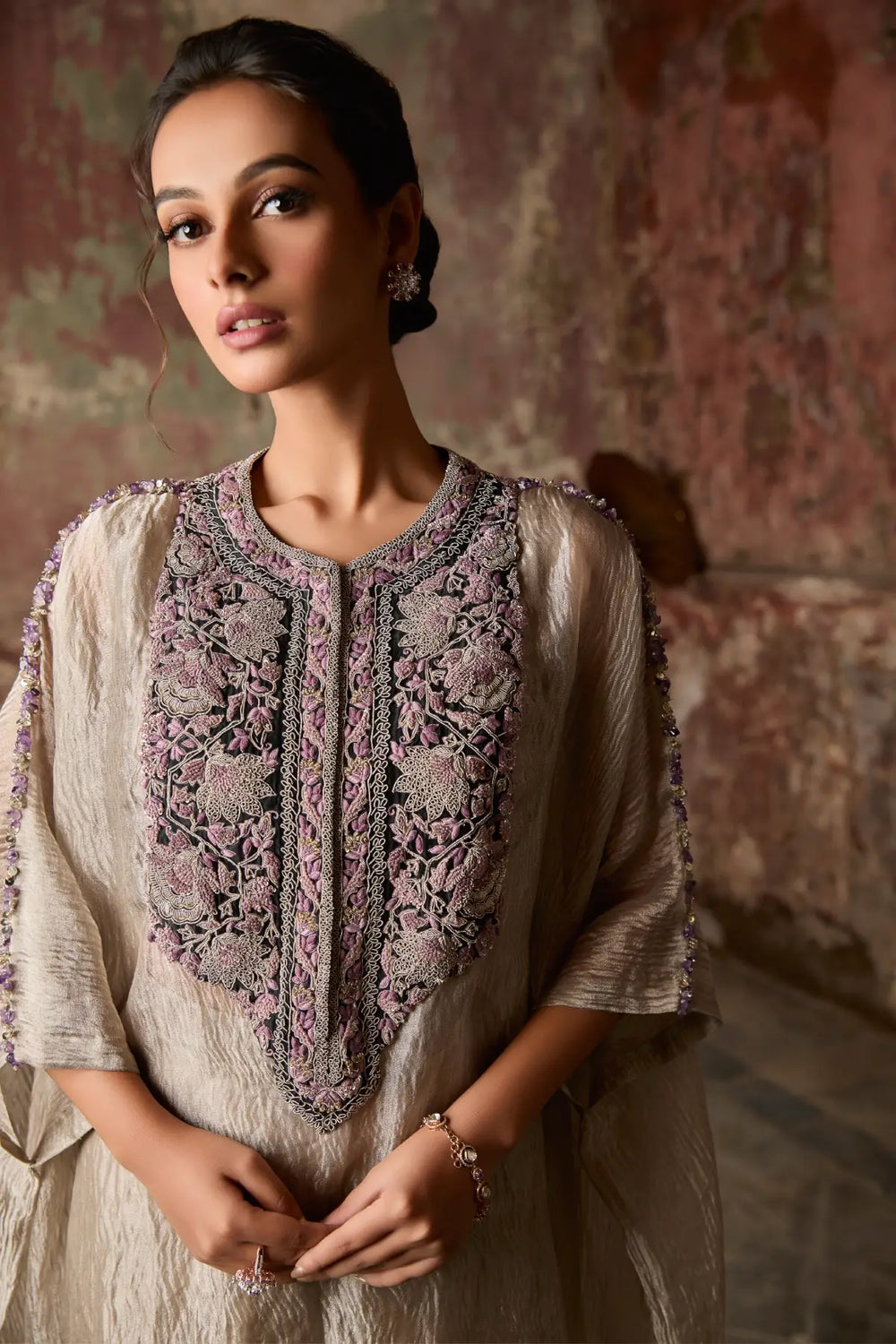 Woman wearing a traditional embroidered kaftan against a textured wall.