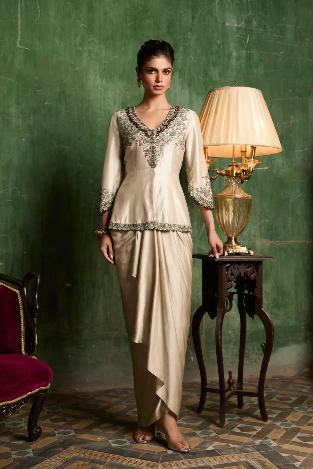 Woman in a formal peplum standing next to a lamp against a green wall.