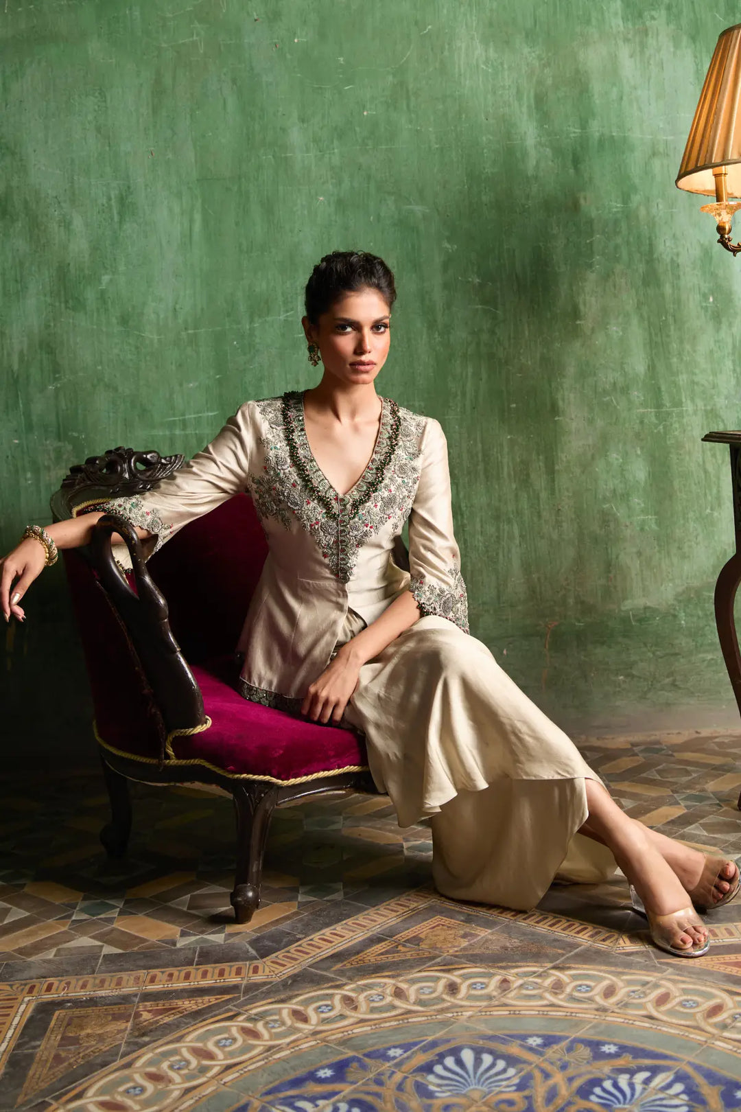 Woman in a traditional peplum sitting on a chair against a green wall.