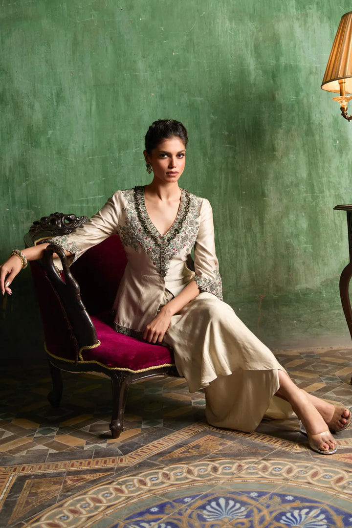 Woman in a traditional peplum sitting on a chair against a green wall.