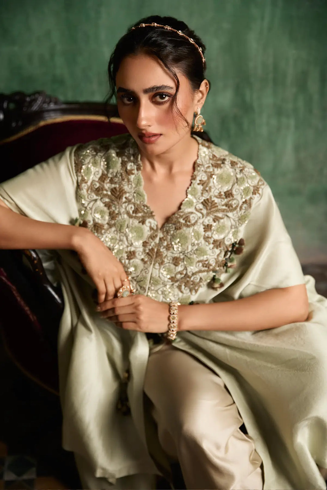 Woman in a floral kaftan and light-colored skirt sitting against a green background