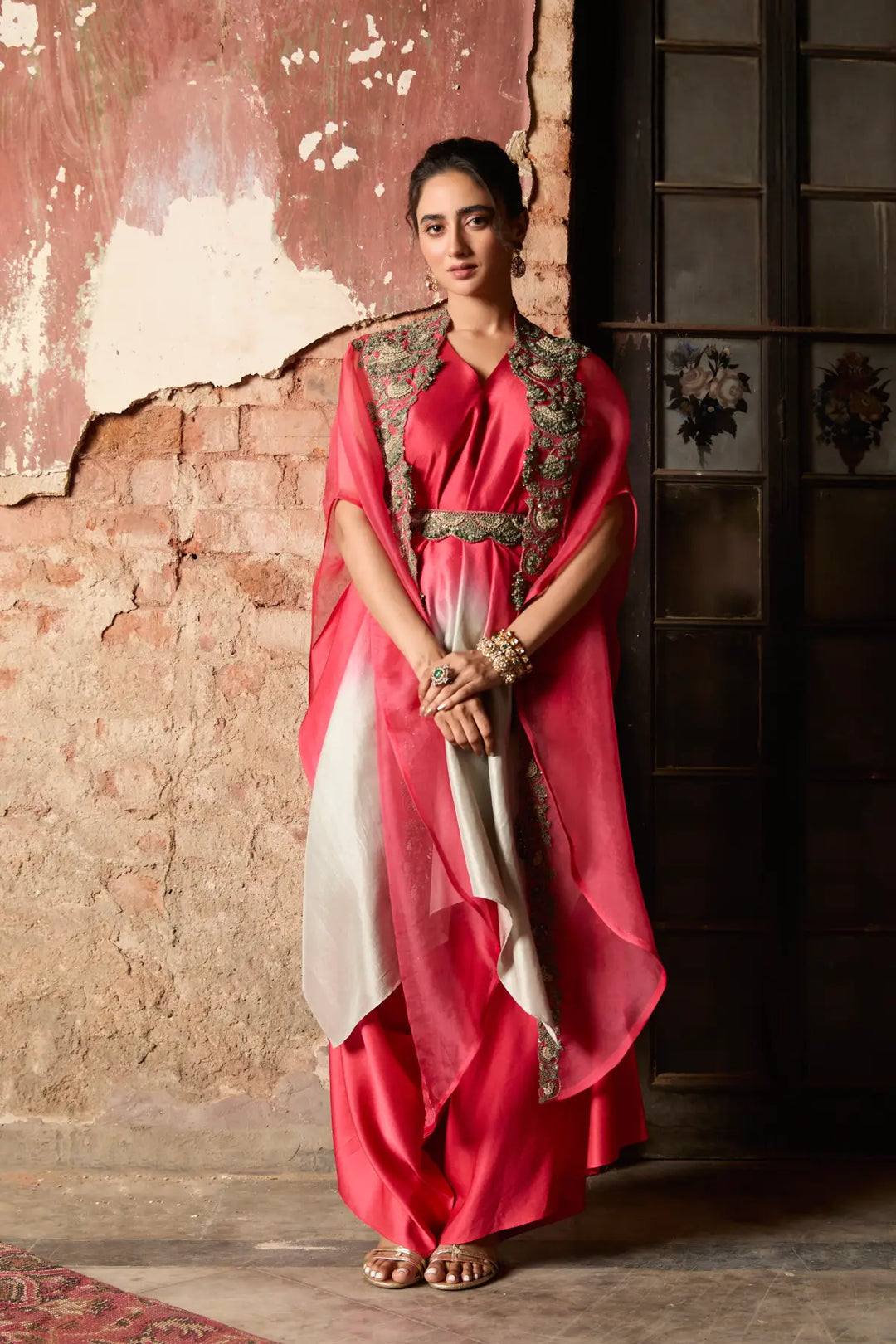 Woman in a red and white traditional cape standing against a textured wall.