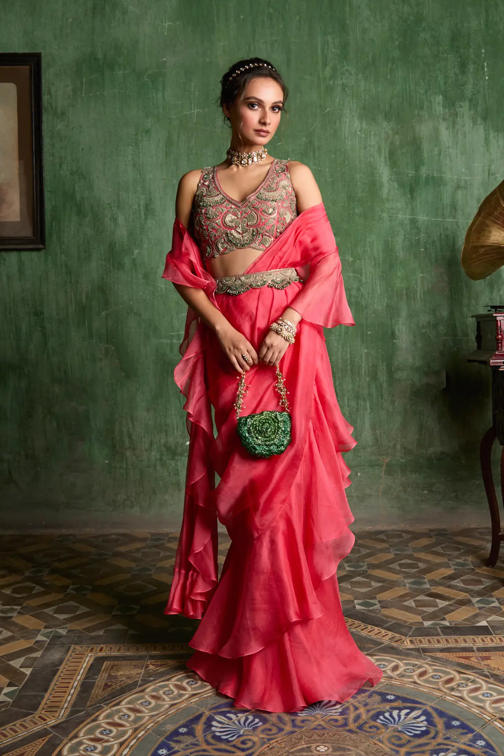 Woman in a pink traditional saree with a green wall and patterned floor.