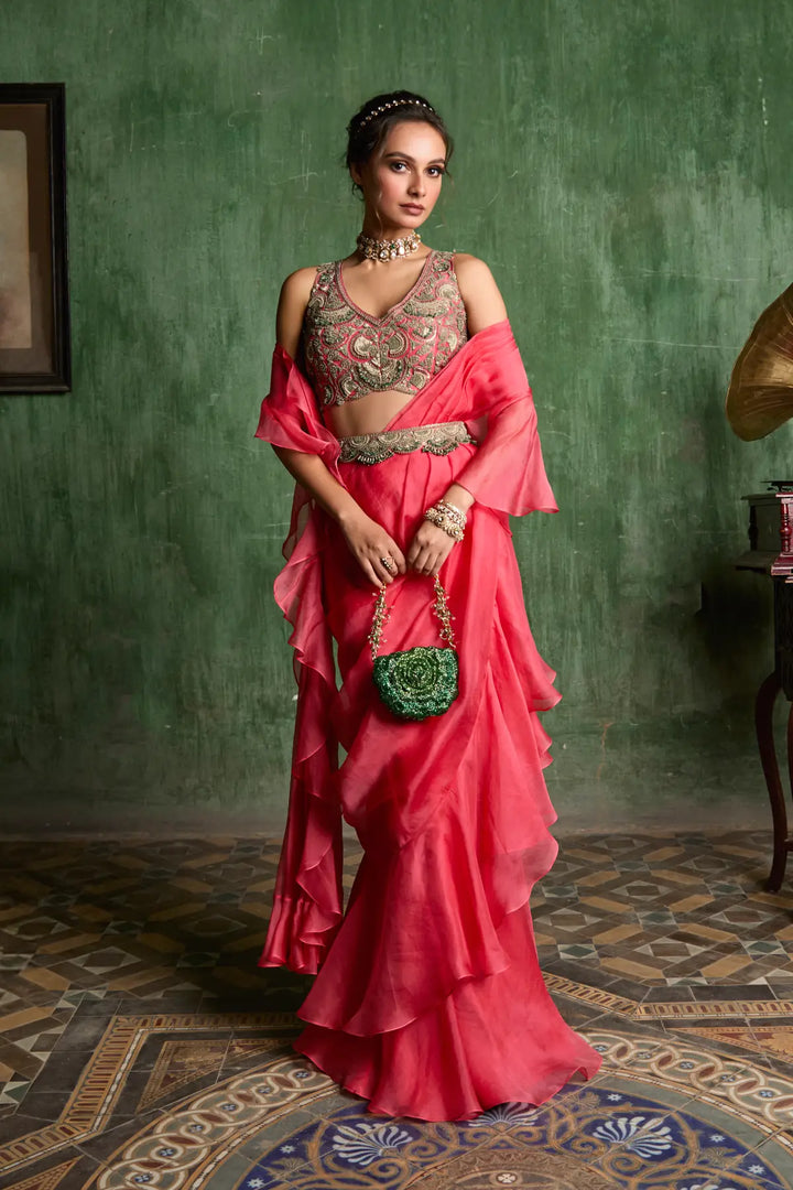 Woman in a pink traditional saree with a green wall and patterned floor.