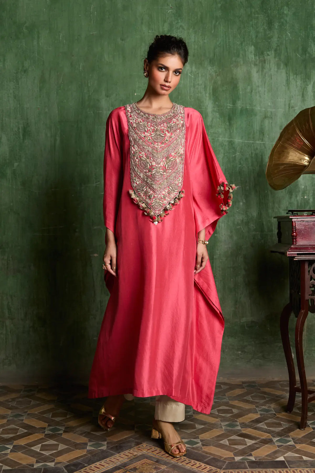 Woman in a pink traditional kaftan with intricate embroidery against a green wall.