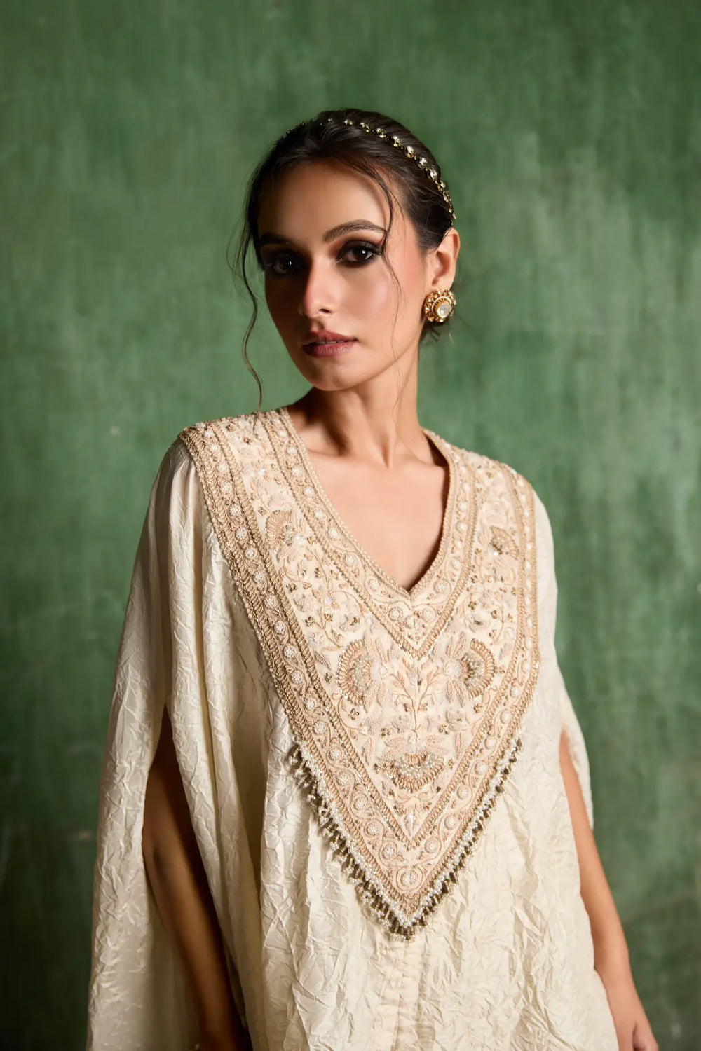 Woman wearing a cream embroidered traditional kaftan against a green background