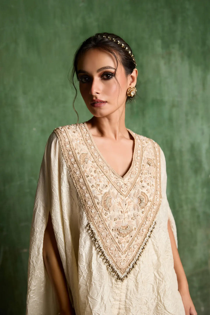 Woman wearing a cream embroidered traditional kaftan against a green background