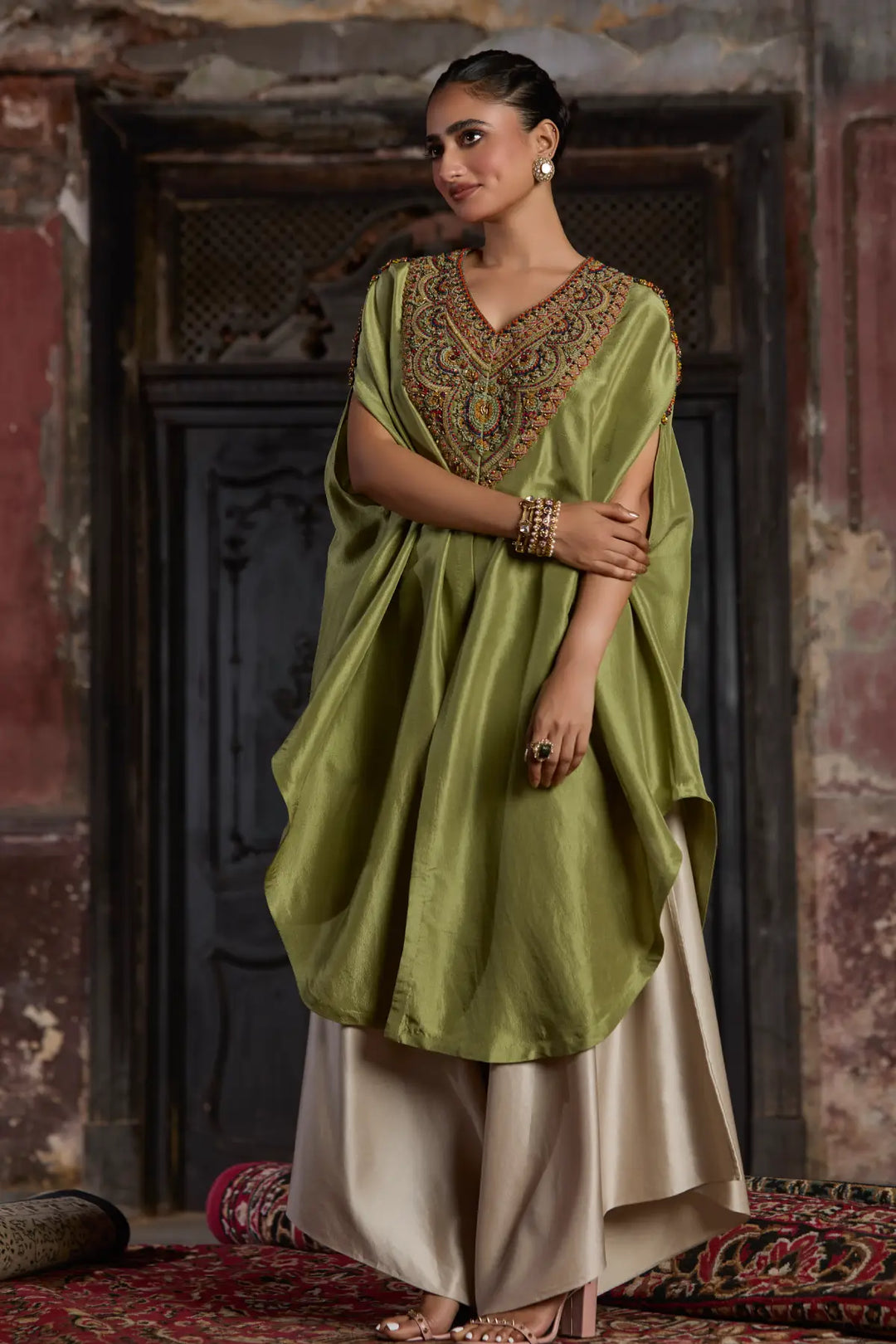 Woman wearing a green and beige traditional kaftan with intricate patterns in a decorative setting.