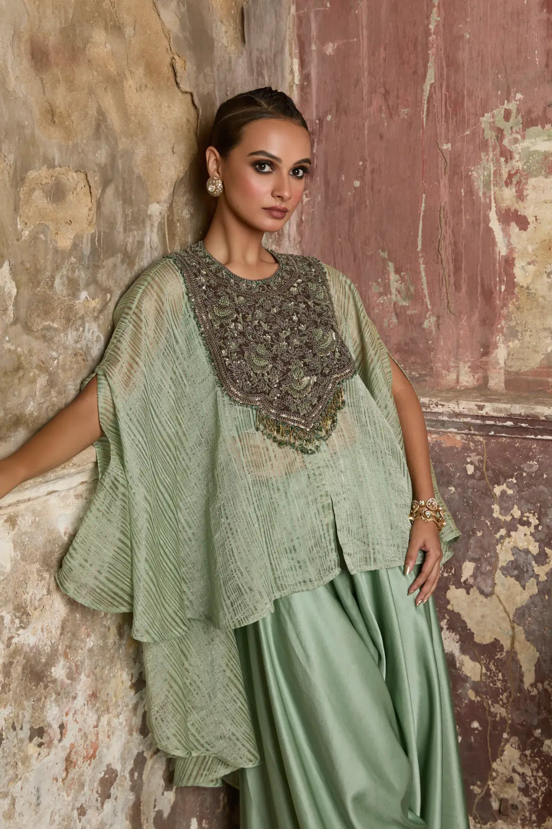 Woman in a green kaftan with intricate detailing against a textured wall.