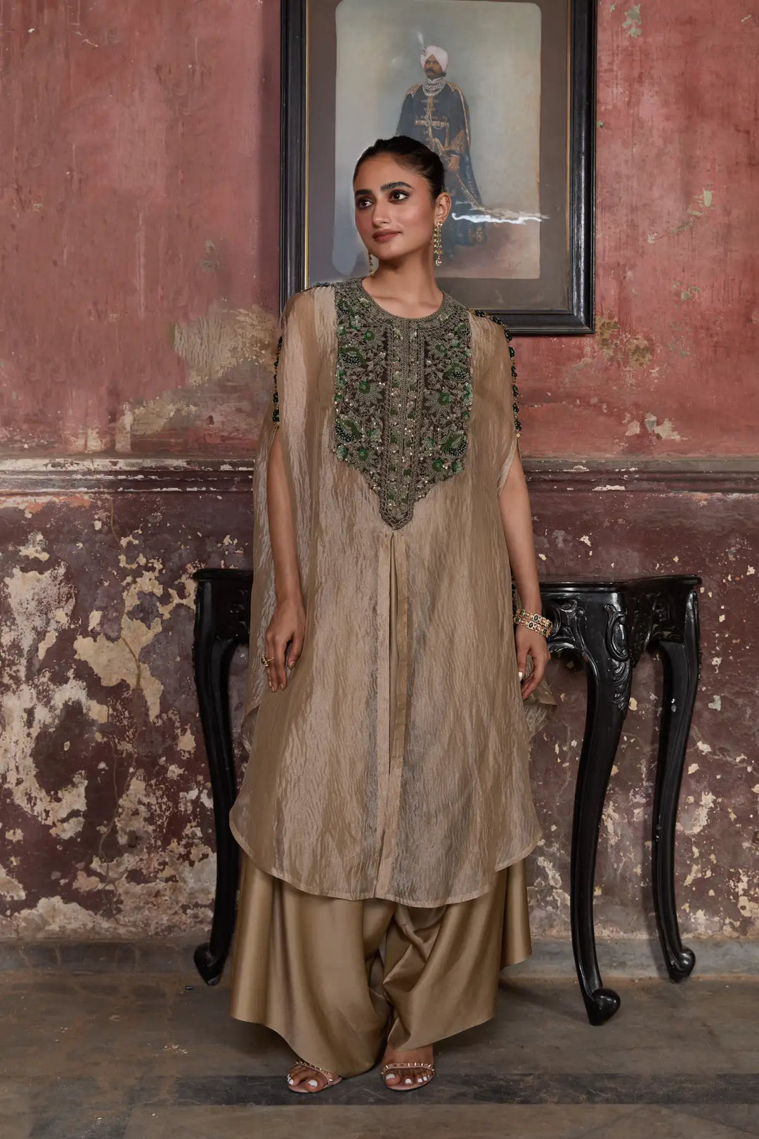 Woman in traditional kaftan standing in a room with a textured wall and framed picture.