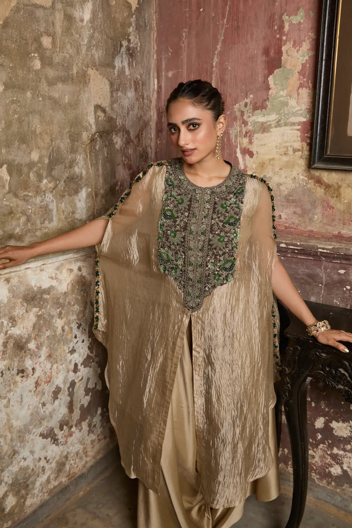Woman in a traditional kaftan standing against a textured wall.