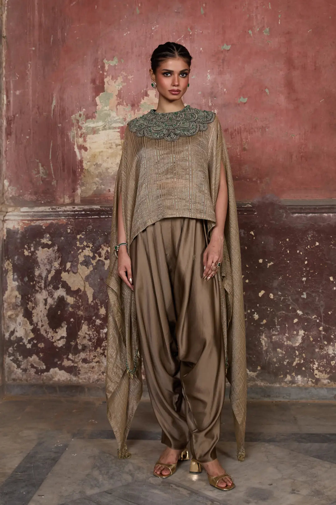 Woman wearing a traditional kaftan with a textured top and flowing pants against a rustic wall.