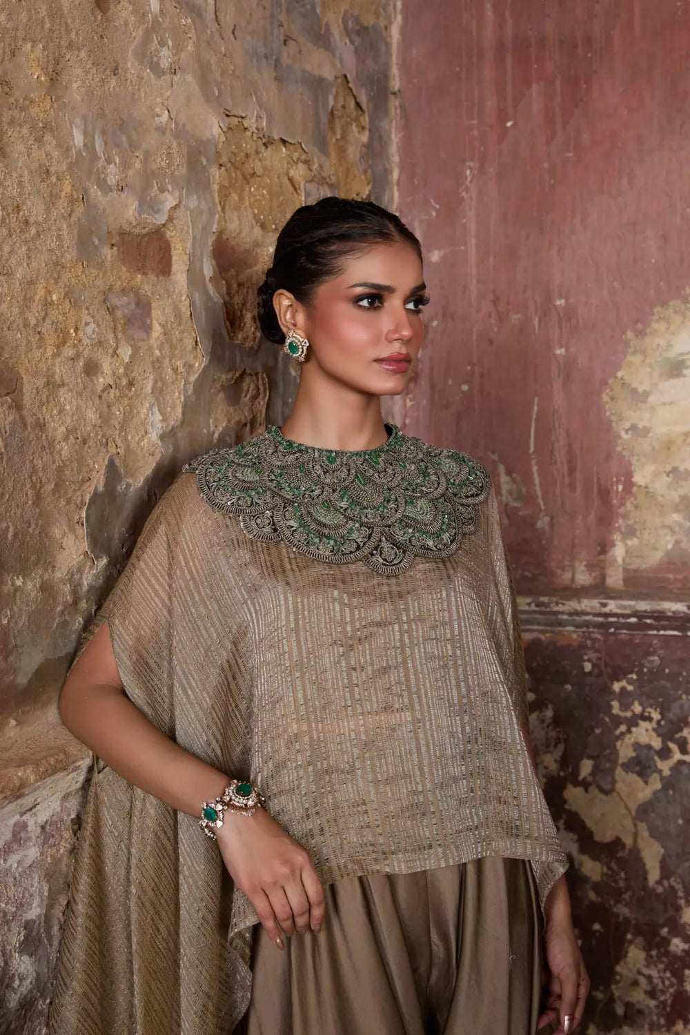 Woman wearing a traditional kaftan with intricate details against a textured wall.