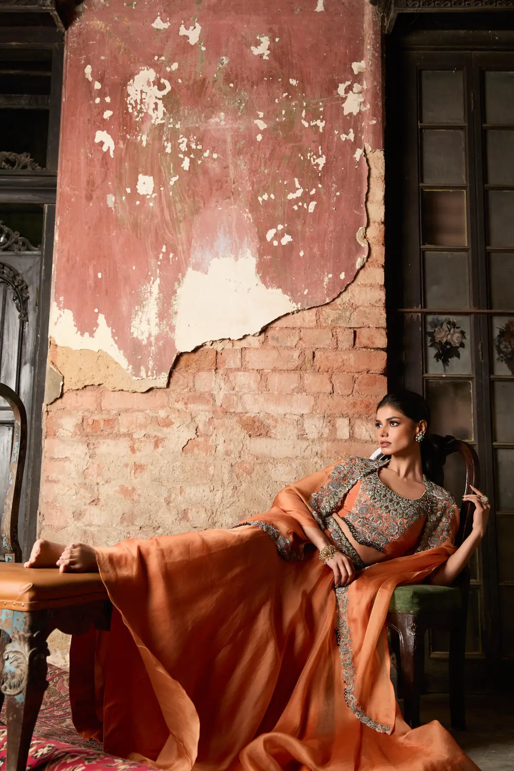 Woman in traditional cape and skirt sitting against a textured wall.