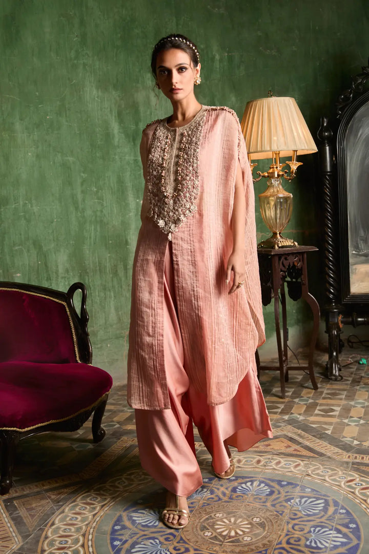 Woman in a pink traditional kaftan standing in an elegant room with a green wall and patterned floor.