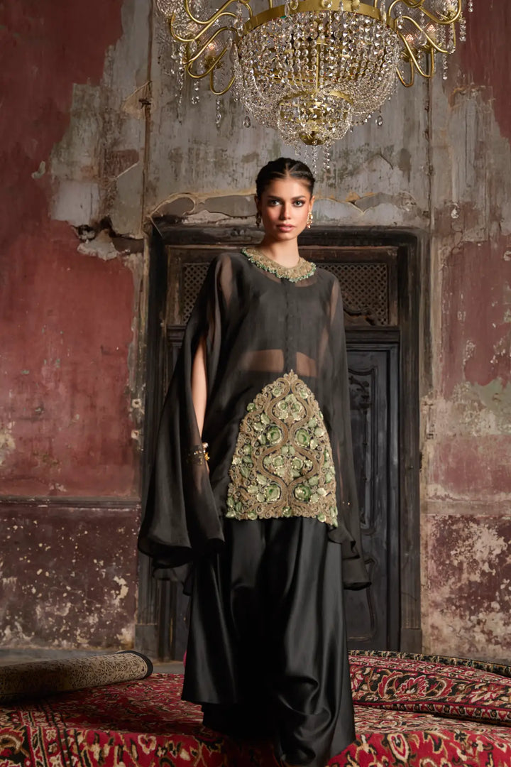 Woman in a black kaftaan with floral patterns standing in an ornate room with a chandelier.