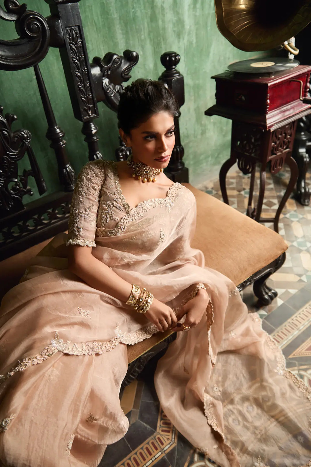 Woman in a traditional saree sitting on an ornate chair with vintage decor.