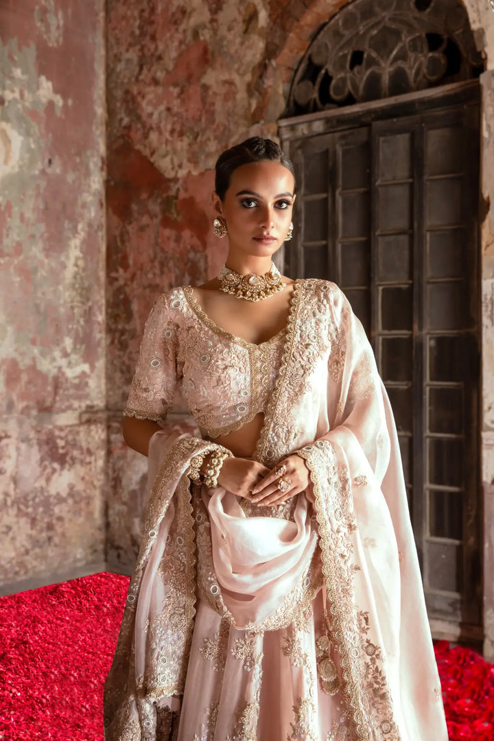 Woman in a traditional lehenga with intricate designs standing against a textured wall.