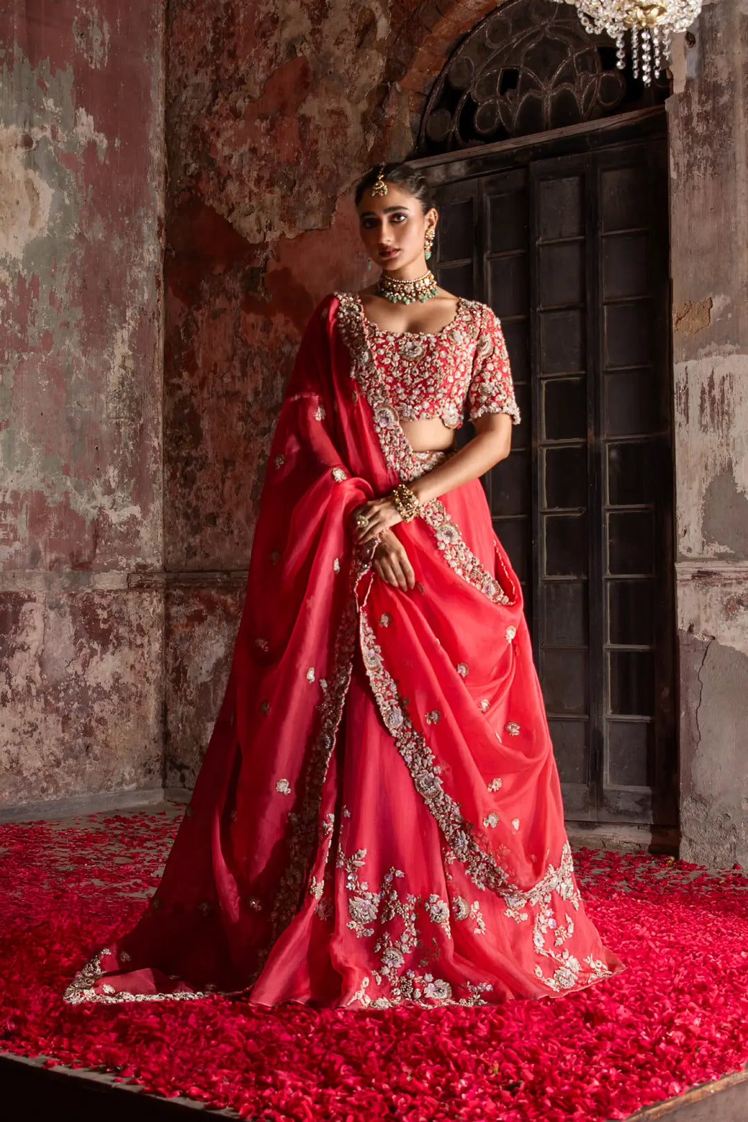 Woman in a red embroidered lehenga standing in an ornate room with chandelier.