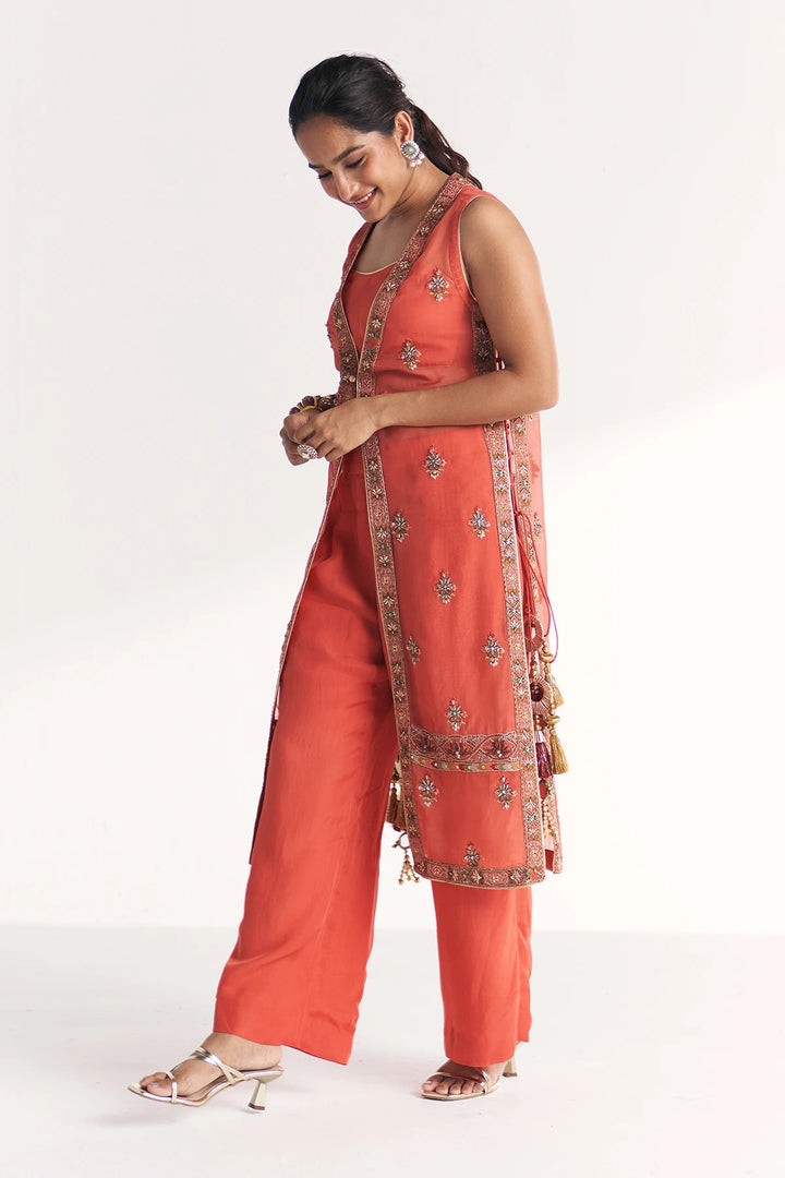 Woman wearing an orange traditional Anarkali with intricate patterns on a white background