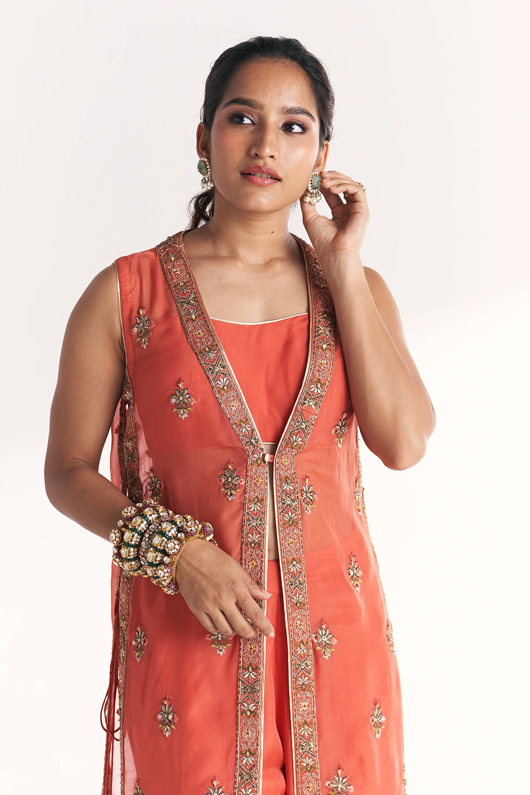 Woman wearing a coral pink traditional Anarkali with intricate designs on a white background