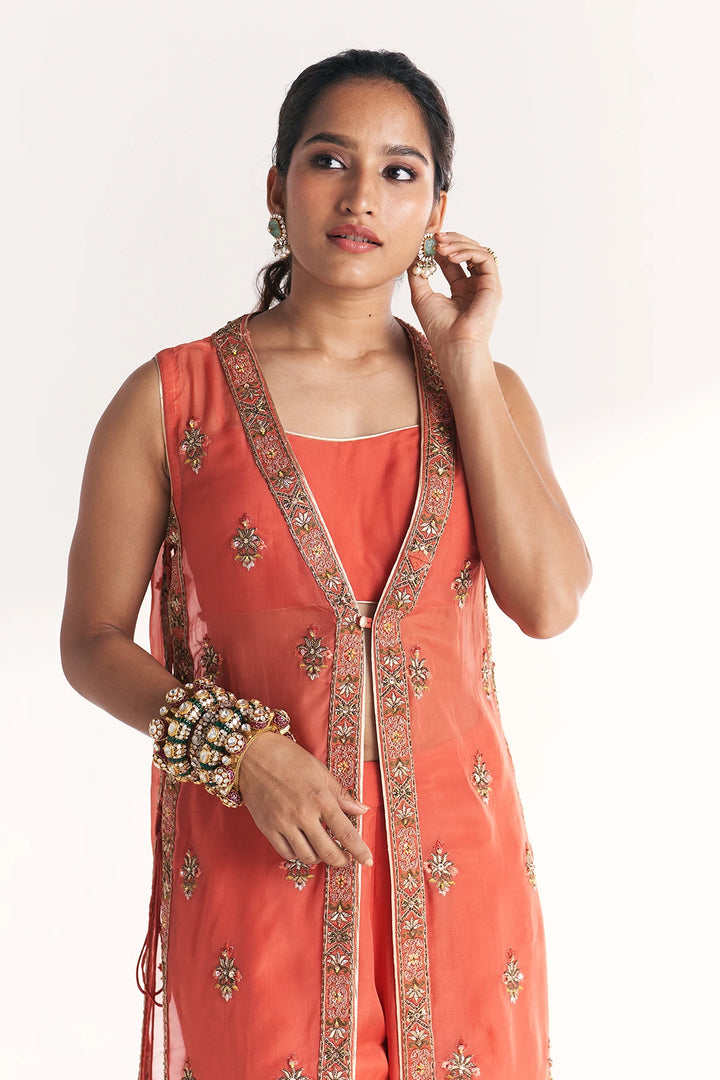 Woman wearing a coral pink traditional Anarkali with intricate designs on a white background