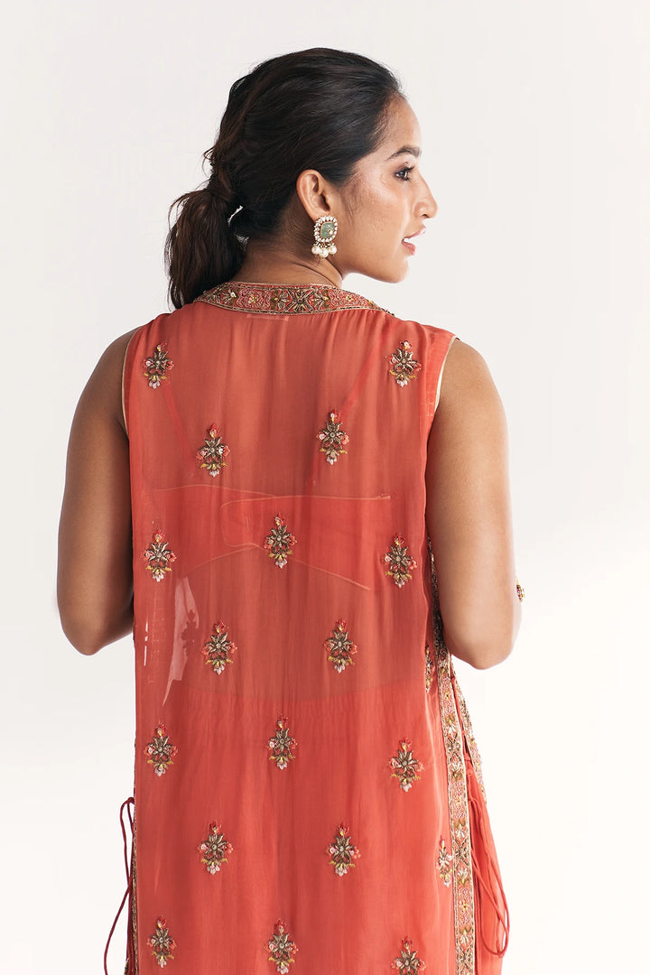 Woman wearing a coral-colored traditional Anarkali with intricate designs on a white background