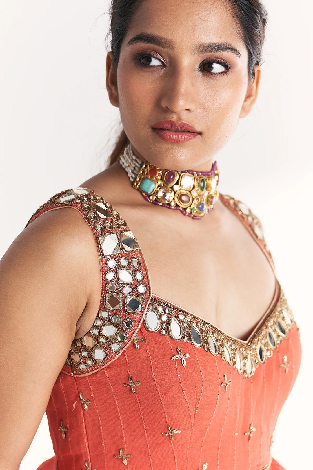 Woman wearing a traditional Anarkali with intricate mirror work and a colorful necklace on a white background