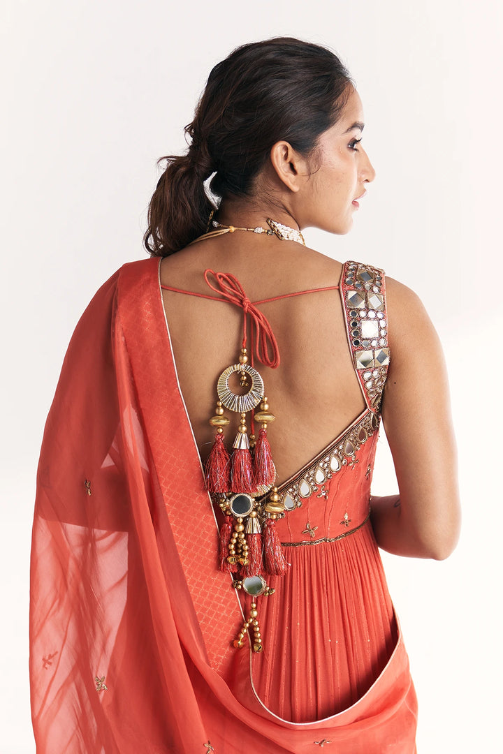 Woman wearing a traditional orange Anarkali with intricate designs and jewellery on a white background