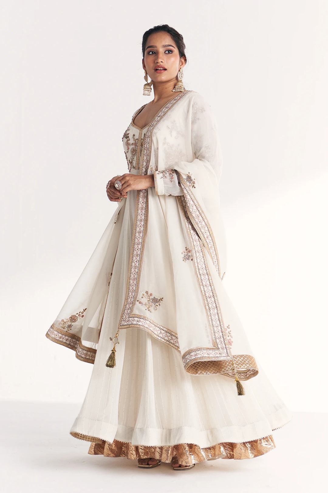 Woman wearing a white traditional Anarkali with gold embroidery on a white background