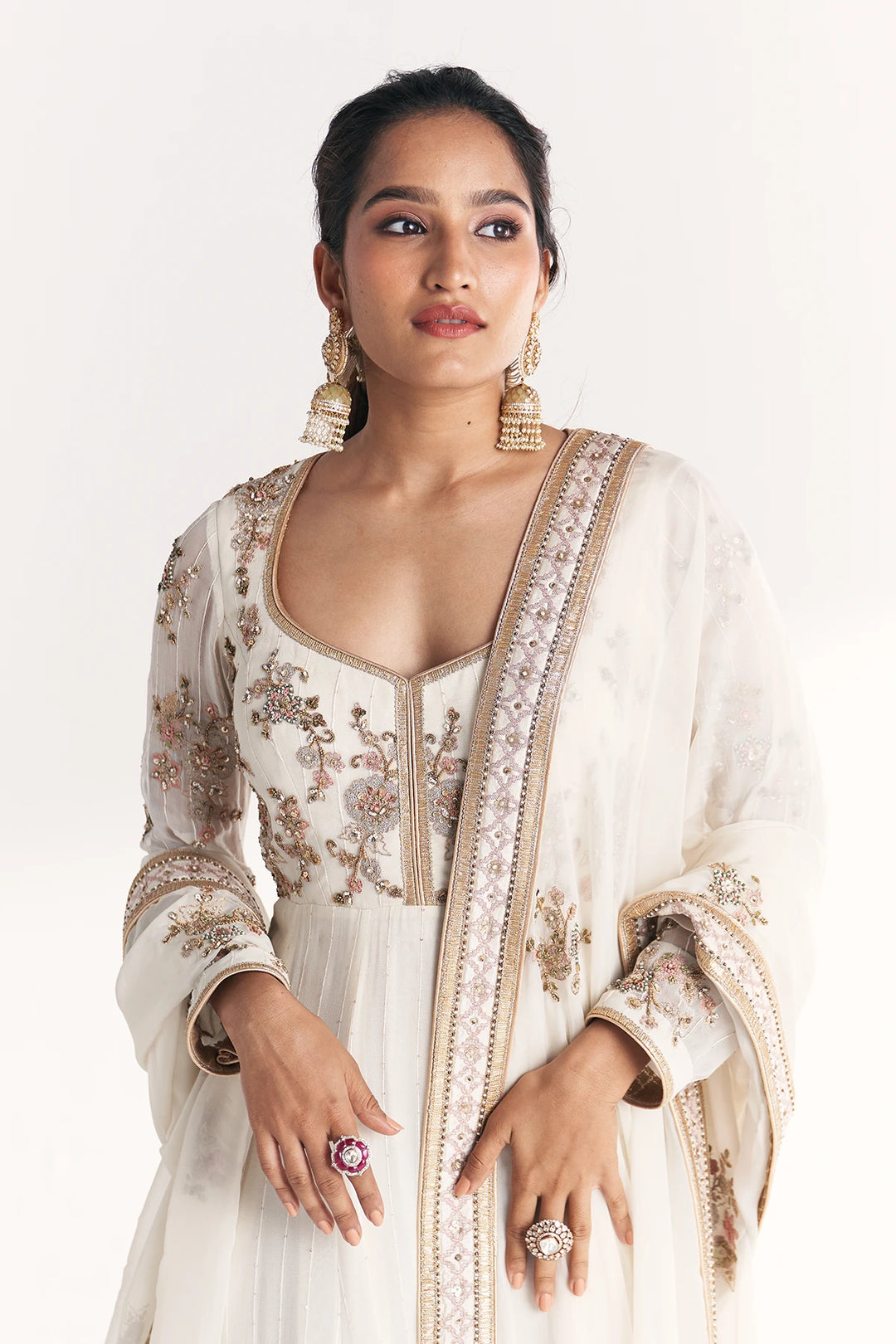 Woman wearing an embroidered white traditional Anarkali with gold details on a white background