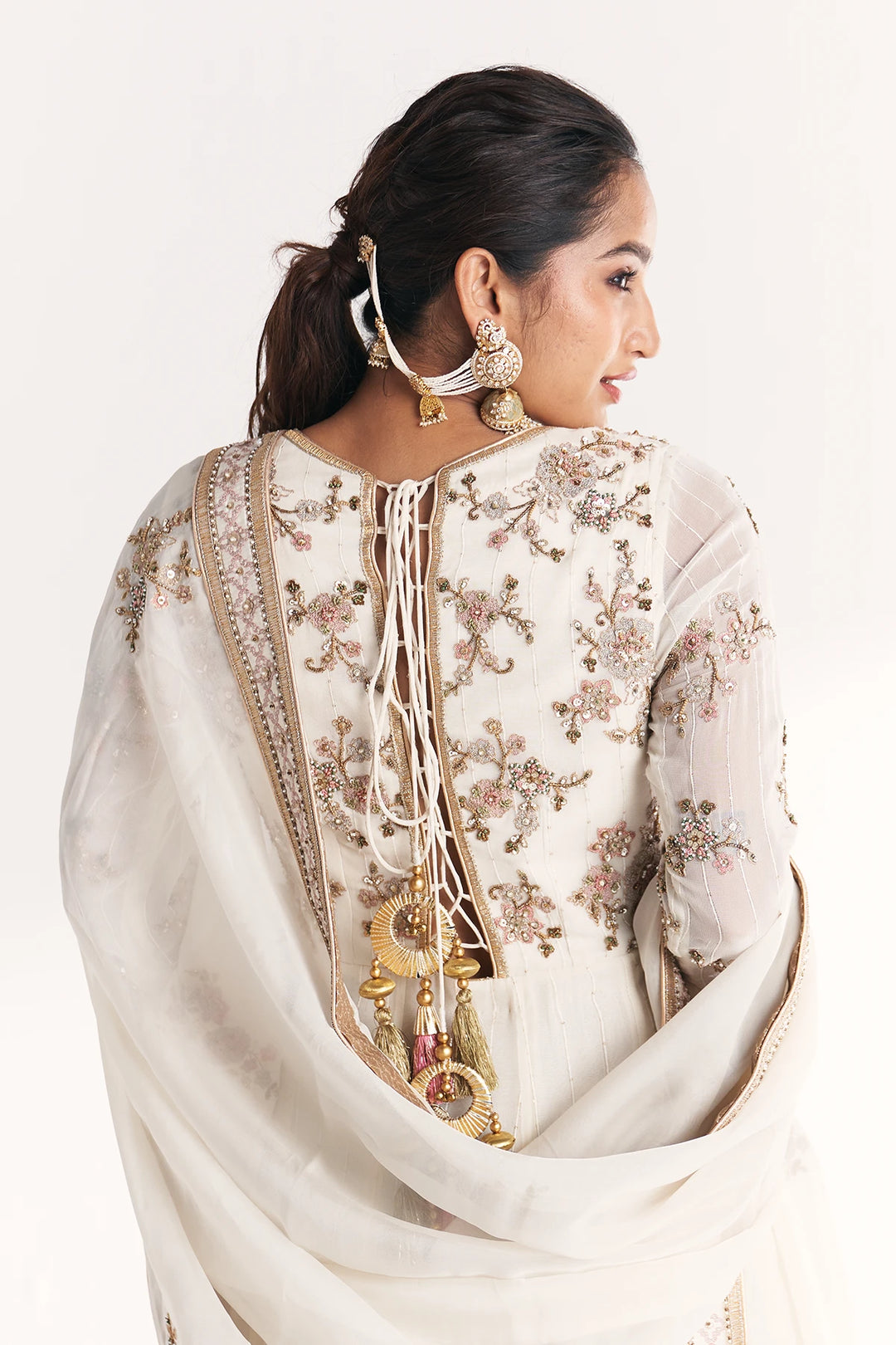 Woman wearing a white embroidered Anarkali with a plain background